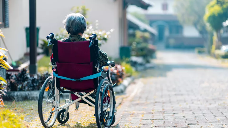Äldre dam i rullstol sitter framför ett hus.Foto