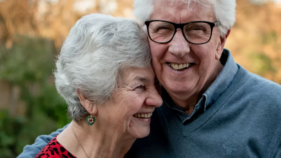 Foto. Ett äldre par som håller om varandra och ler