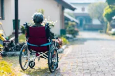 Äldre dam i rullstol sitter framför ett hus.Foto